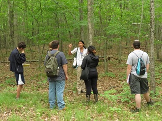 Nora Mitchell standing in a forest facing four students who are watching her talk